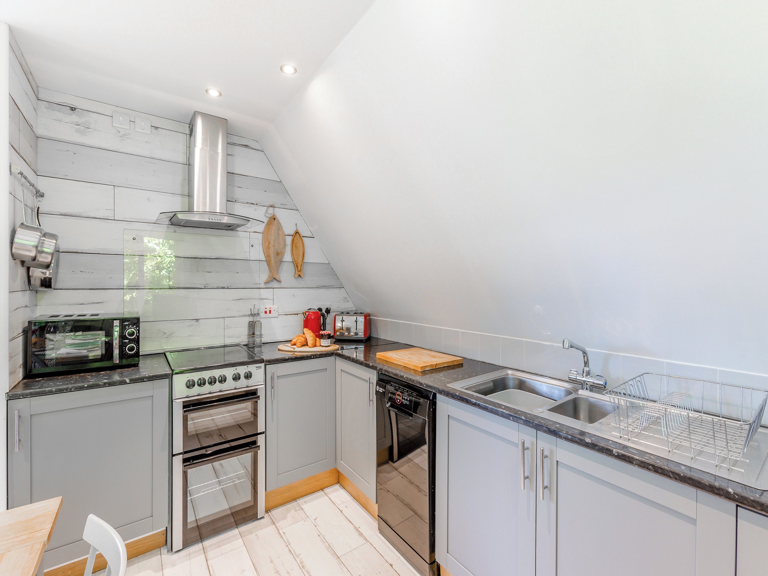 A compact kitchen with a gas stove, a built-in oven, a dishwasher, and a small countertop with a toaster and a cutting board.