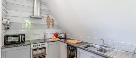 A compact kitchen with a gas stove, a built-in oven, a dishwasher, and a small countertop with a toaster and a cutting board.