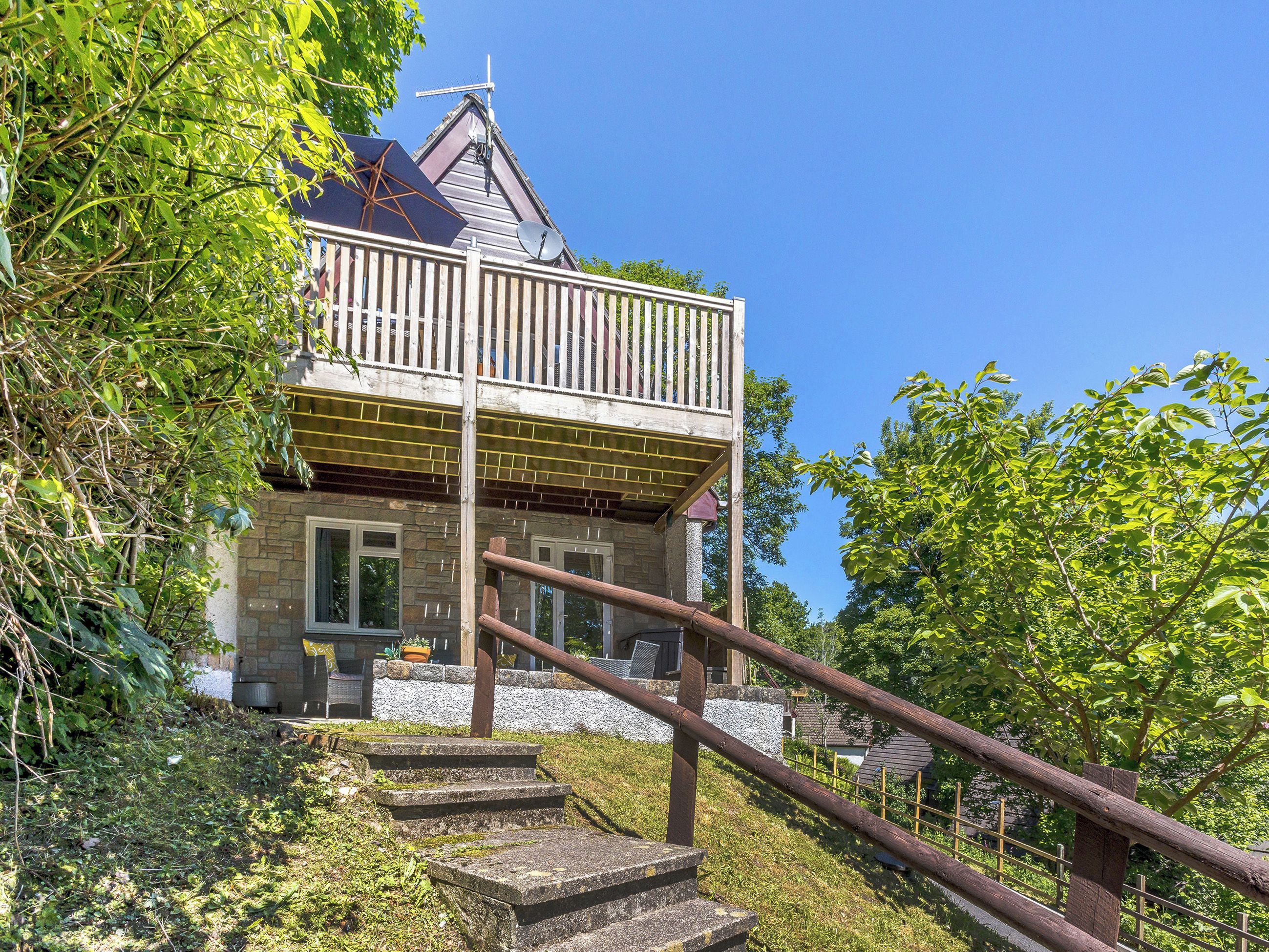 A two-story house with a balcony, stone exterior, and a wooden staircase leading to the entrance.