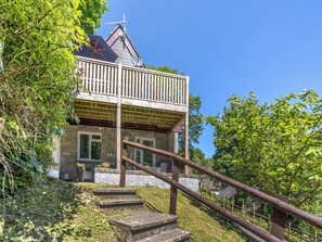 A two-story house with a balcony, stone exterior, and a wooden staircase leading to the entrance.
