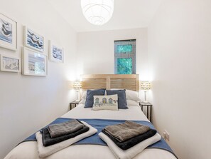 A neatly made bed with a headboard, two bedside lamps, and a window with blinds.