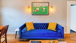 A blue sofa with yellow cushions, a framed comic strip, and a book on a wooden table.