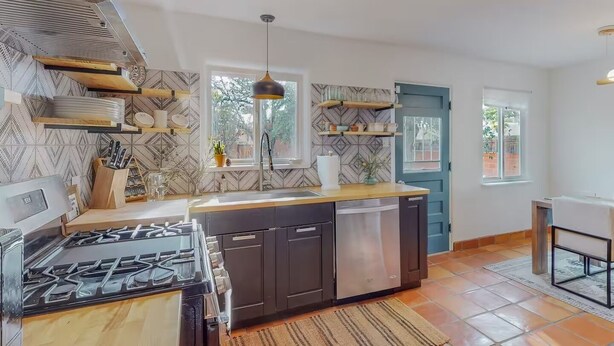 A modern kitchen with a gas stove, dishwasher, and wooden countertops. There are shelves with dishes and a window providing natural light. - Stylish 2bd/1ba + Office & Yard (Albuquerque)