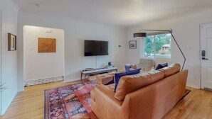A modern living room with a leather sofa, a flat-screen TV, a desk with a computer, and a patterned rug. - Stylish 2bd/1ba + Office & Yard (Albuquerque)