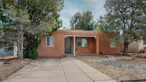 A single-story house with a flat roof, a front door, and a small porch. - Stylish 2bd/1ba + Office & Yard (Albuquerque)