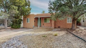 A single-story house with a flat roof, a front porch, and a green door. - Stylish 2bd/1ba + Office & Yard (Albuquerque)