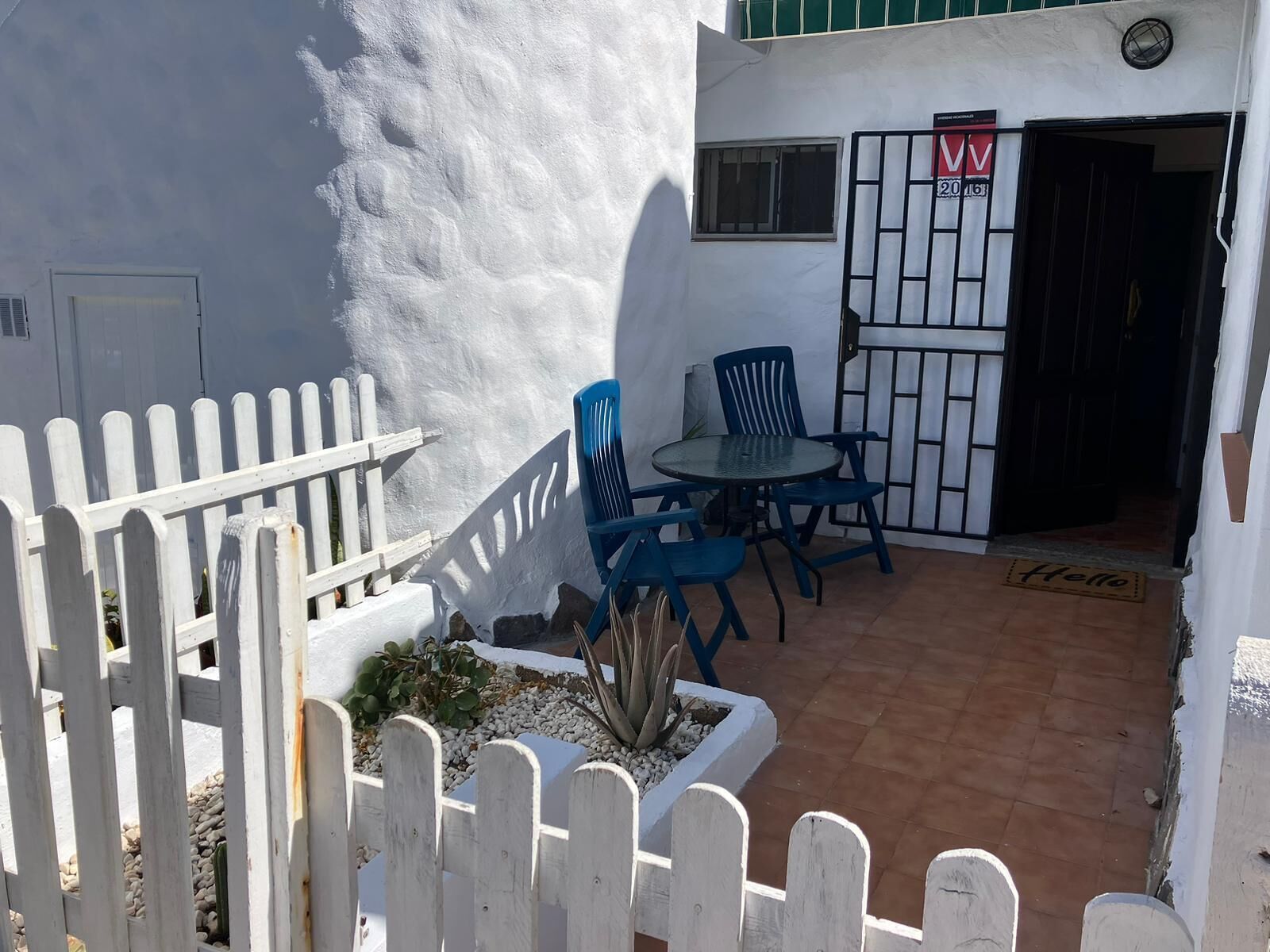 Een terras met een witte hek, een kleine tafel en blauwe stoelen.