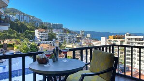 A balcony with a table, chairs, and a view of a coastal cityscape.