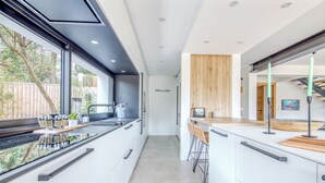 A modern kitchen with a central island, a window with a view of greenery, and a wooden accent wall. - La Canopèa: The Art of Living in Cap Ferret, Between the Pine Forest and the Ocean (Lège-Cap-Ferret)