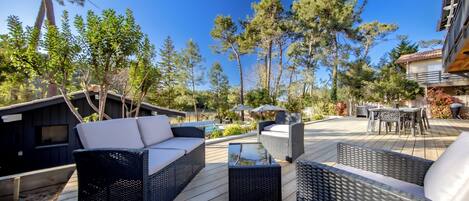 An outdoor patio with wicker furniture, a pool, and a view of trees and a building.