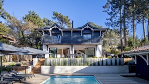 A modern two-story house with a pool, outdoor seating, and a balcony. - La Canopèa: The Art of Living in Cap Ferret, Between the Pine Forest and the Ocean (Lège-Cap-Ferret)