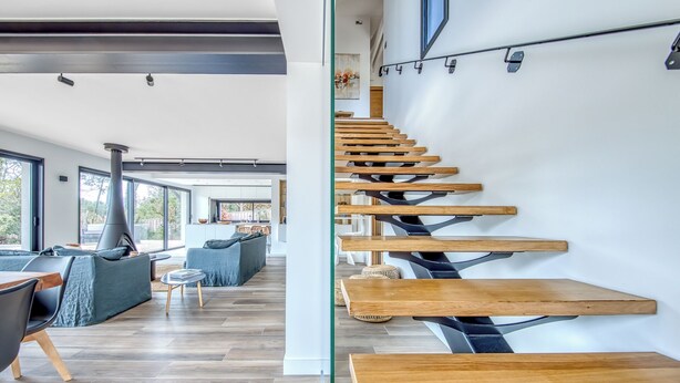 A modern interior with a wooden staircase, a dining area, and a kitchen in the background. - La Canopèa: The Art of Living in Cap Ferret, Between the Pine Forest and the Ocean (Lège-Cap-Ferret)