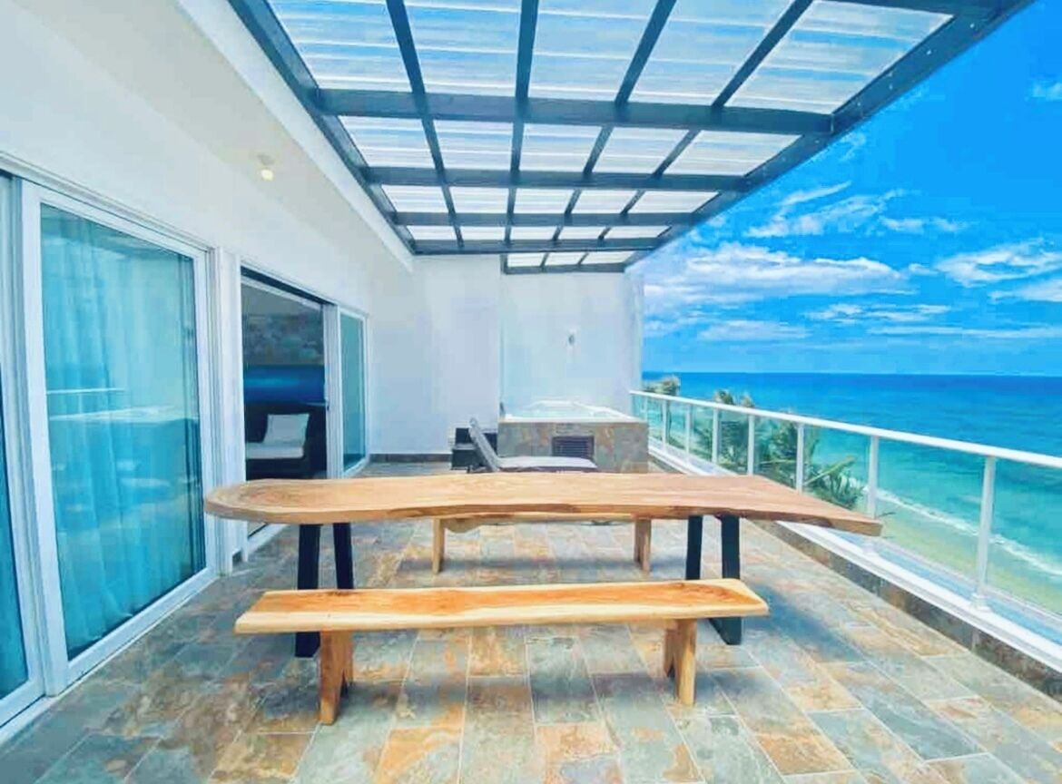 A balcony with a wooden table and bench, overlooking the ocean.