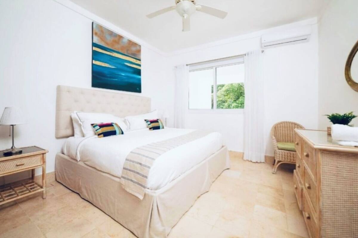 A bedroom with a bed, bedside table, dresser, and a window with curtains.