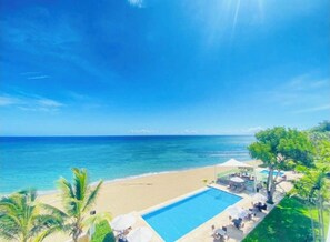A beachside pool area with clear blue water, a sandy beach, and palm trees. - Blue Green (Sosúa)