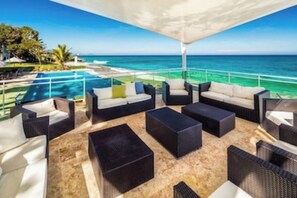 Un espace de détente extérieur, baigné de lumière, avec piscine et vue sur l’océan, aménagé avec des canapés et des fauteuils.