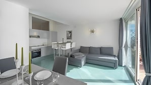 A modern living room with a grey sofa, dining table with chairs, and a kitchen area in the background.