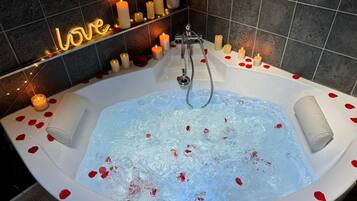 A bathtub filled with water and rose petals, surrounded by candles and a neon sign that reads "love".