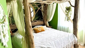Una cama con dosel, paredes verdes y una planta colgante.