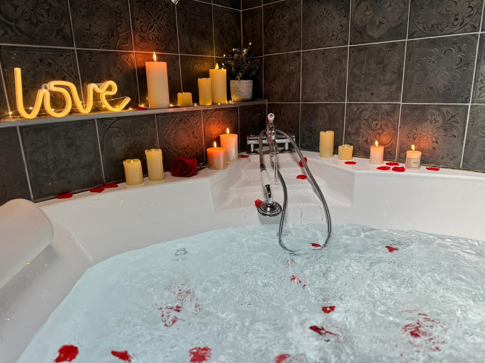 Un baño con bañera, varias velas y un letrero de neón que dice 'love'.
