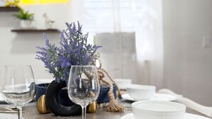 A dining table set with white plates, glasses, and cutlery, a vase with purple flowers, and a decorative rope.