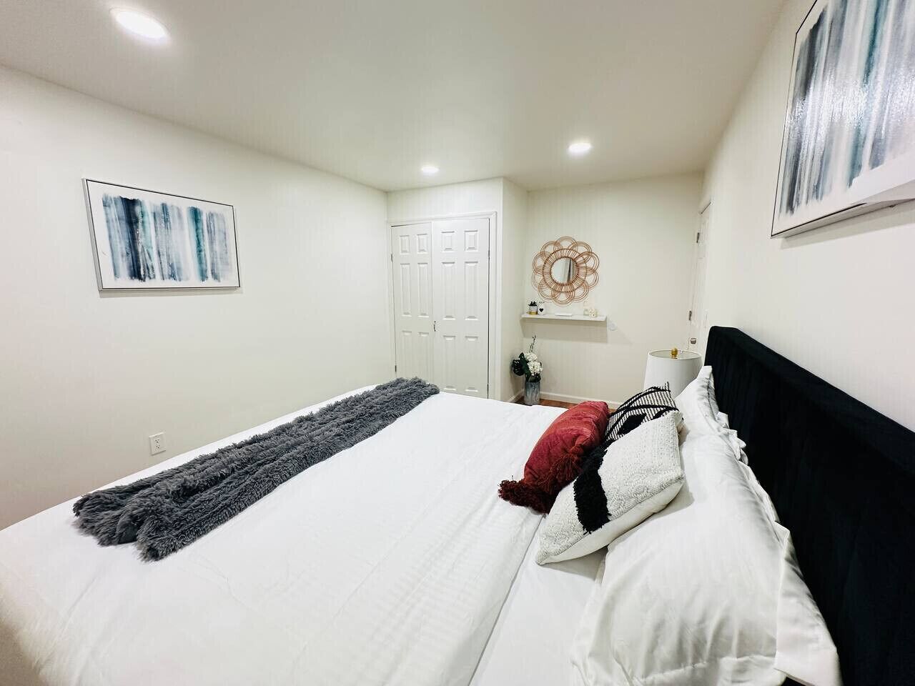 A bedroom with a bed, a door, a wall-mounted artwork, a small table with a vase, and a wall decoration.