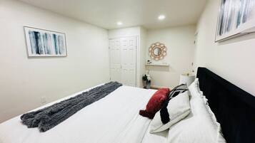 A bedroom with a bed, a door, a wall-mounted artwork, a small table with a vase, and a wall decoration.