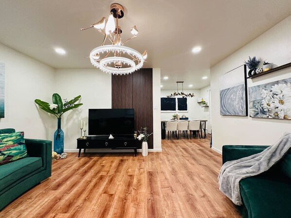 A modern living room with a wooden floor, a black entertainment unit, a green sofa, and a chandelier.
