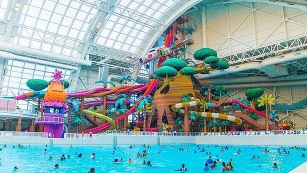 An indoor water park with a large pool, slides, and a climbing structure.
