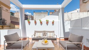 A sunlit patio with a white pergola, two cushioned chairs, a small table with a tray of orange juice, and potted plants on the pergola. - Skandiloft - Holiday rental Malaga city (Málaga)
