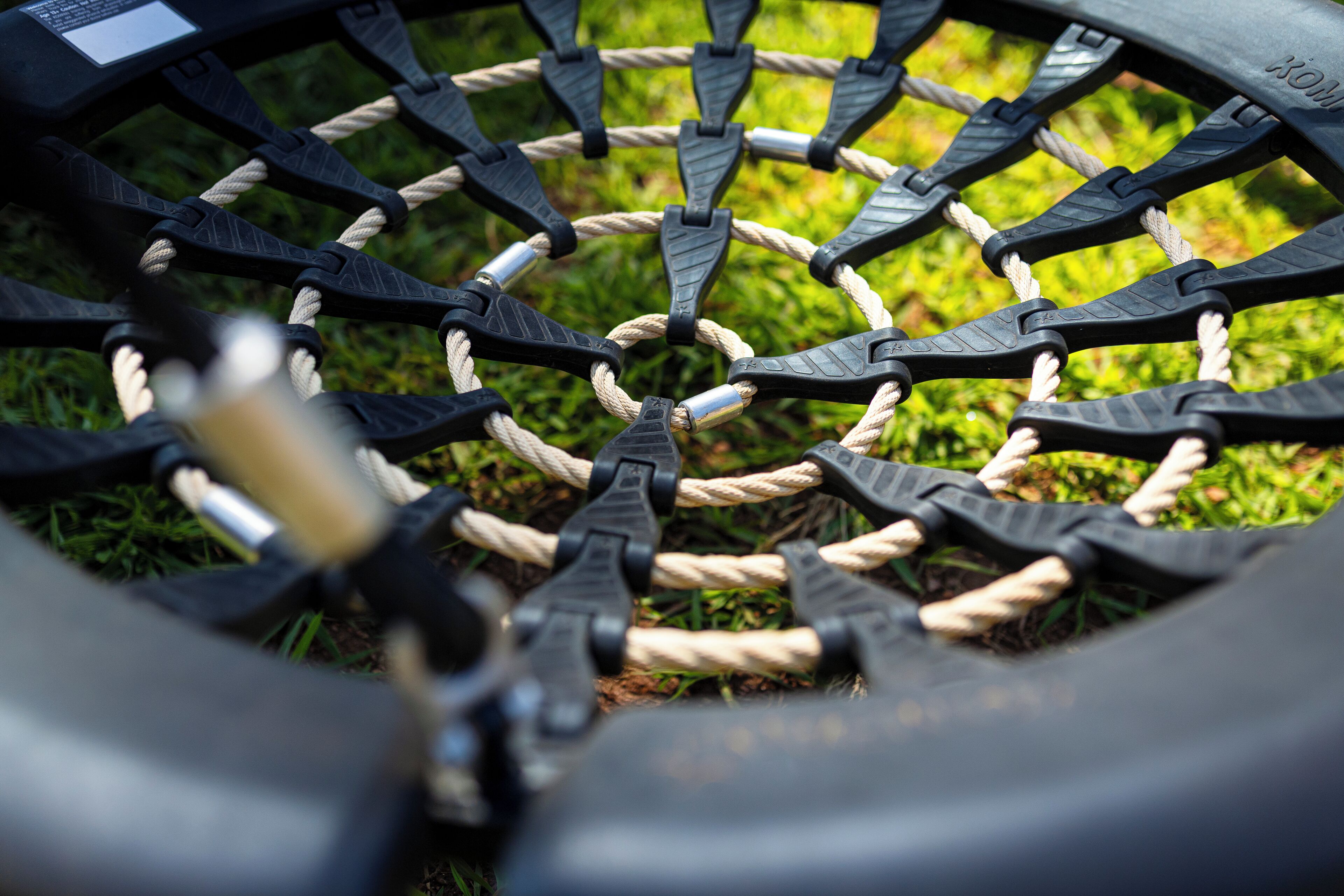 A close-up of a tire with a black metal rim and a rope wrapped around it, set against a grassy background.