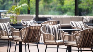 Wicker chairs with striped cushions arranged around tables on an outdoor patio with a view of greenery. - Zaria Court Kigali, Tapestry Collection by Hilton (Kigali)