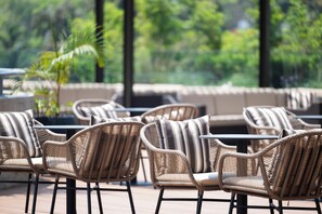 Wicker chairs with striped cushions arranged around tables on an outdoor patio with a view of greenery. - Zaria Court Kigali, Tapestry Collection by Hilton (Kigali)