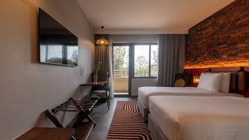 A hotel room with a large bed, a desk, a chair, a TV, and a view of the outdoors.