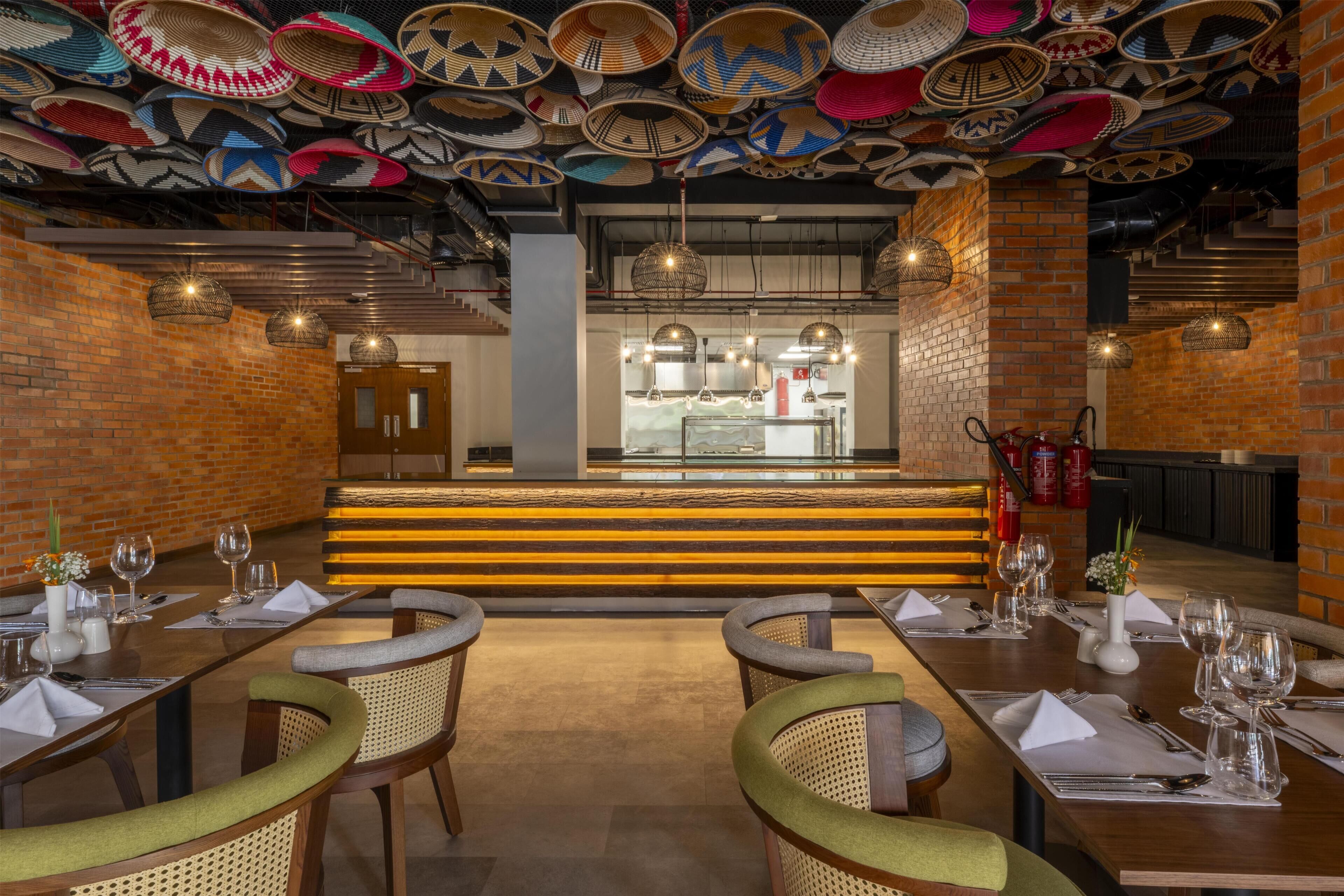 A restaurant interior with brick walls, hanging woven baskets, and a central bar area.