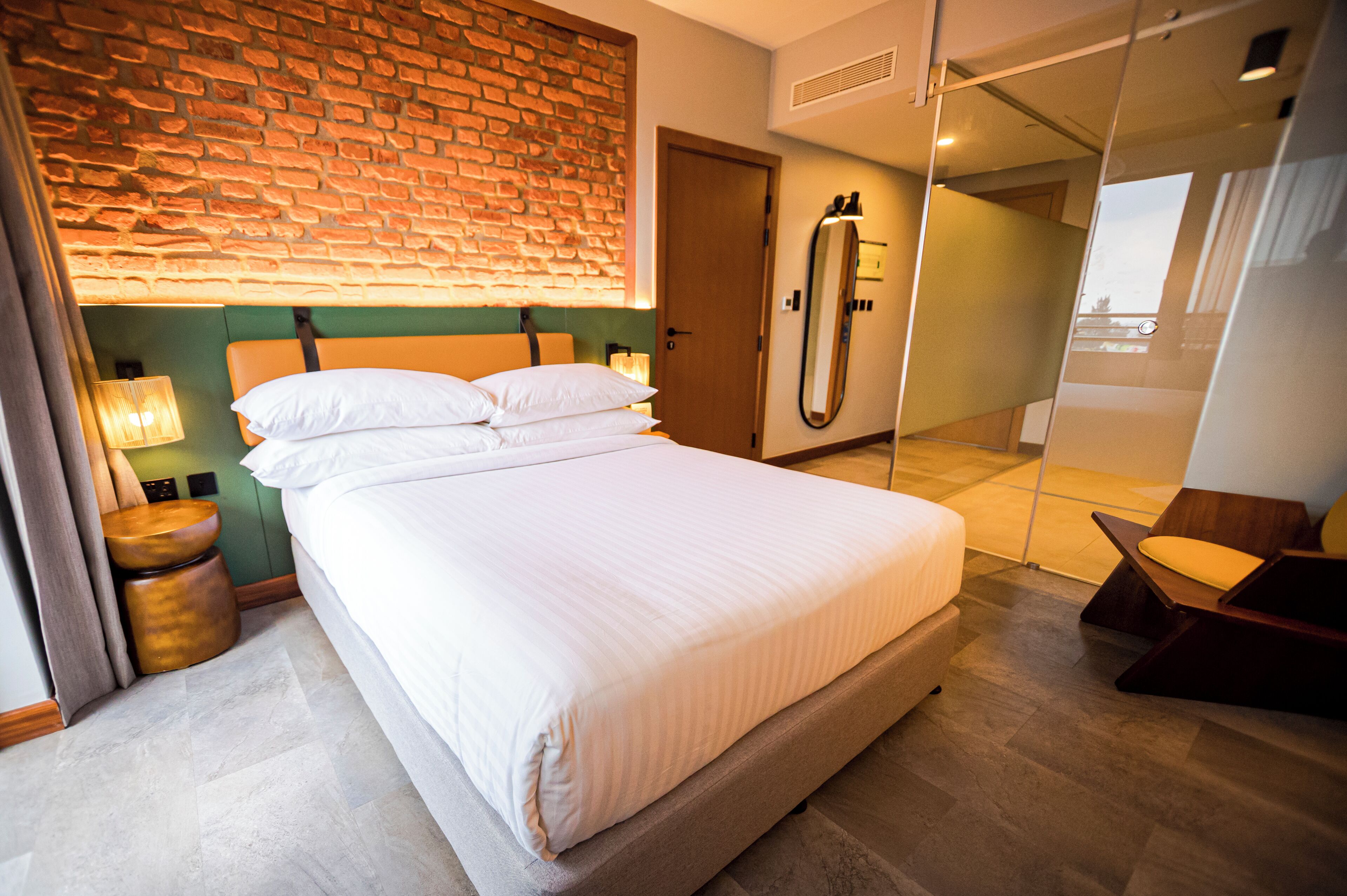 Quarto de hotel com cama, abajures, um espelho e vista através de uma porta de vidro.