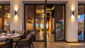 A restaurant with a modern interior, featuring a mix of seating arrangements including tables and booths, and a visible kitchen area in the background. - Zaria Court Kigali, Tapestry Collection by Hilton (Kigali)