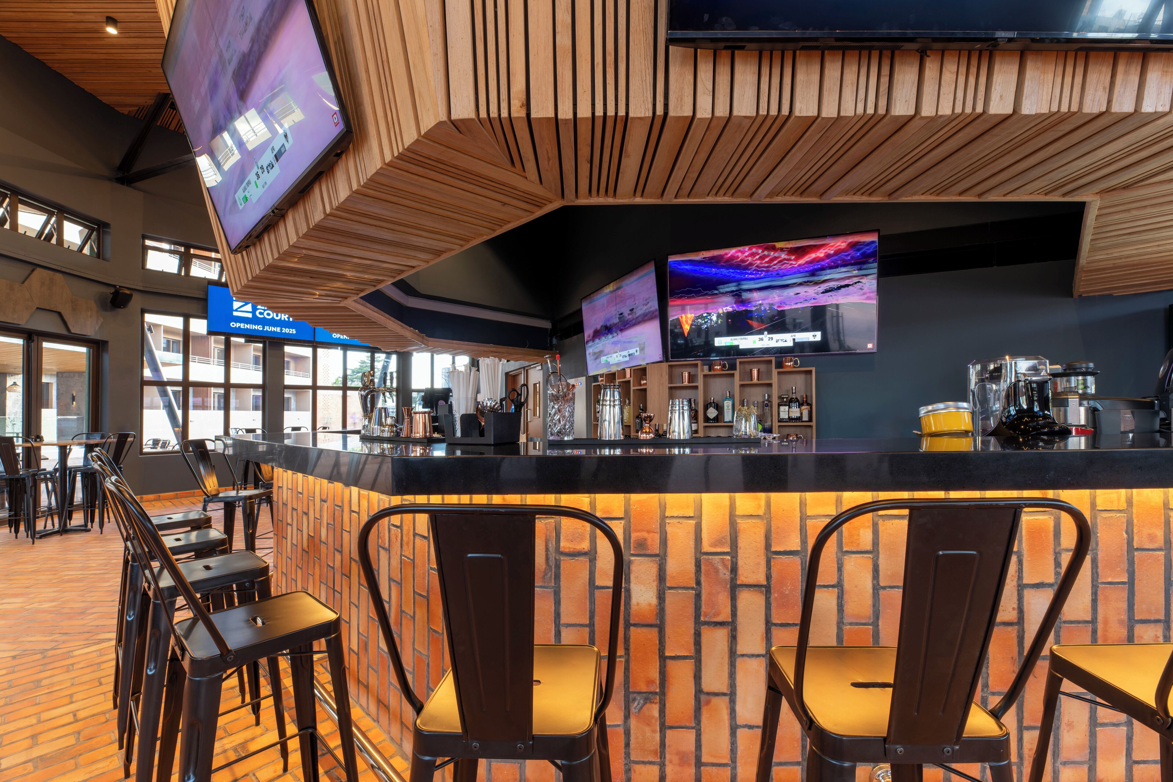 A modern bar area with a brick wall, wooden ceiling, and multiple TVs.