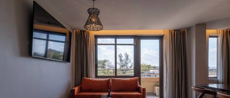 A modern living room with a sofa, two armchairs, a coffee table, and a dining table. Large windows offer a view of the outdoors.