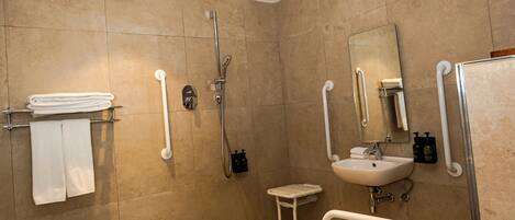 A modern bathroom with a shower, toilet, and sink, equipped with grab bars and a handrail.
