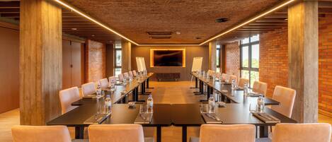 Un salón de conferencias con mesas largas, sillas y una pantalla grande al frente.