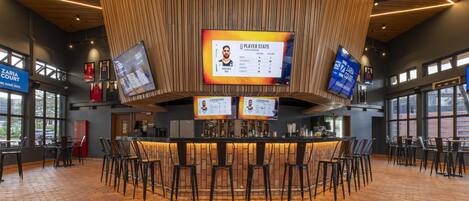 A sports bar with a central counter, multiple screens displaying player stats, and a brick floor.