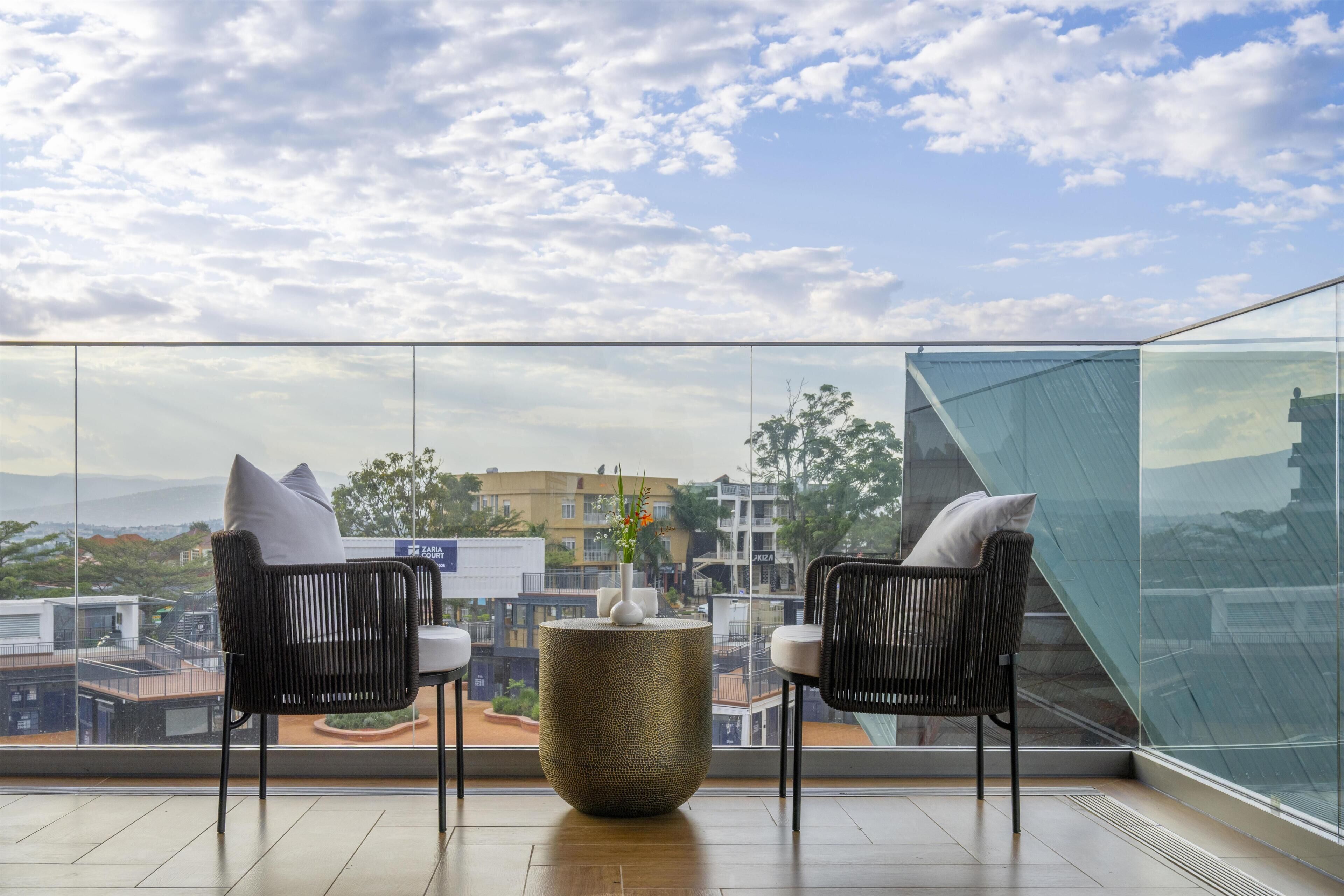 A balcony with two wicker chairs, a textured table, and a clear view of the cityscape.