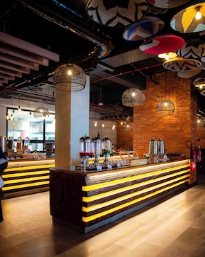 A modern bar area with a central counter, hanging pendant lights, and a brick wall backdrop. - Zaria Court Kigali, Tapestry Collection by Hilton (Kigali)
