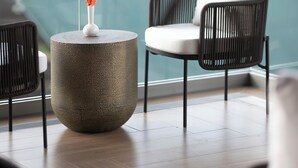 Un área de descanso moderna con una mesa redonda texturizada, una silla blanca acolchada y un jarrón con flores.