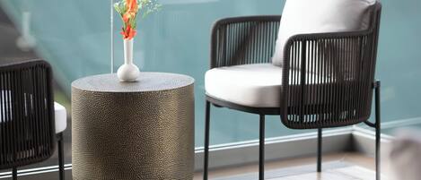 Un área de descanso moderna con una mesa redonda texturizada, una silla blanca acolchada y un jarrón con flores.