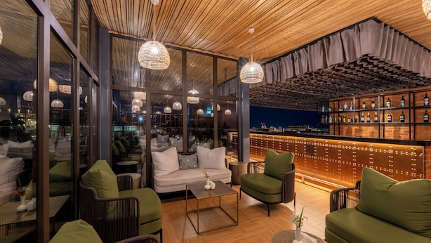 A modern bar area with a wooden ceiling, glass partitions, and a bar stocked with bottles. - Zaria Court Kigali, Tapestry Collection by Hilton (Kigali)