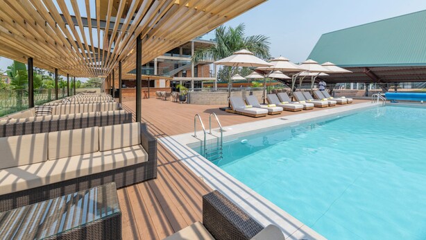 A poolside area with lounge chairs, umbrellas, and a wooden deck. - Zaria Court Kigali, Tapestry Collection by Hilton (Kigali)