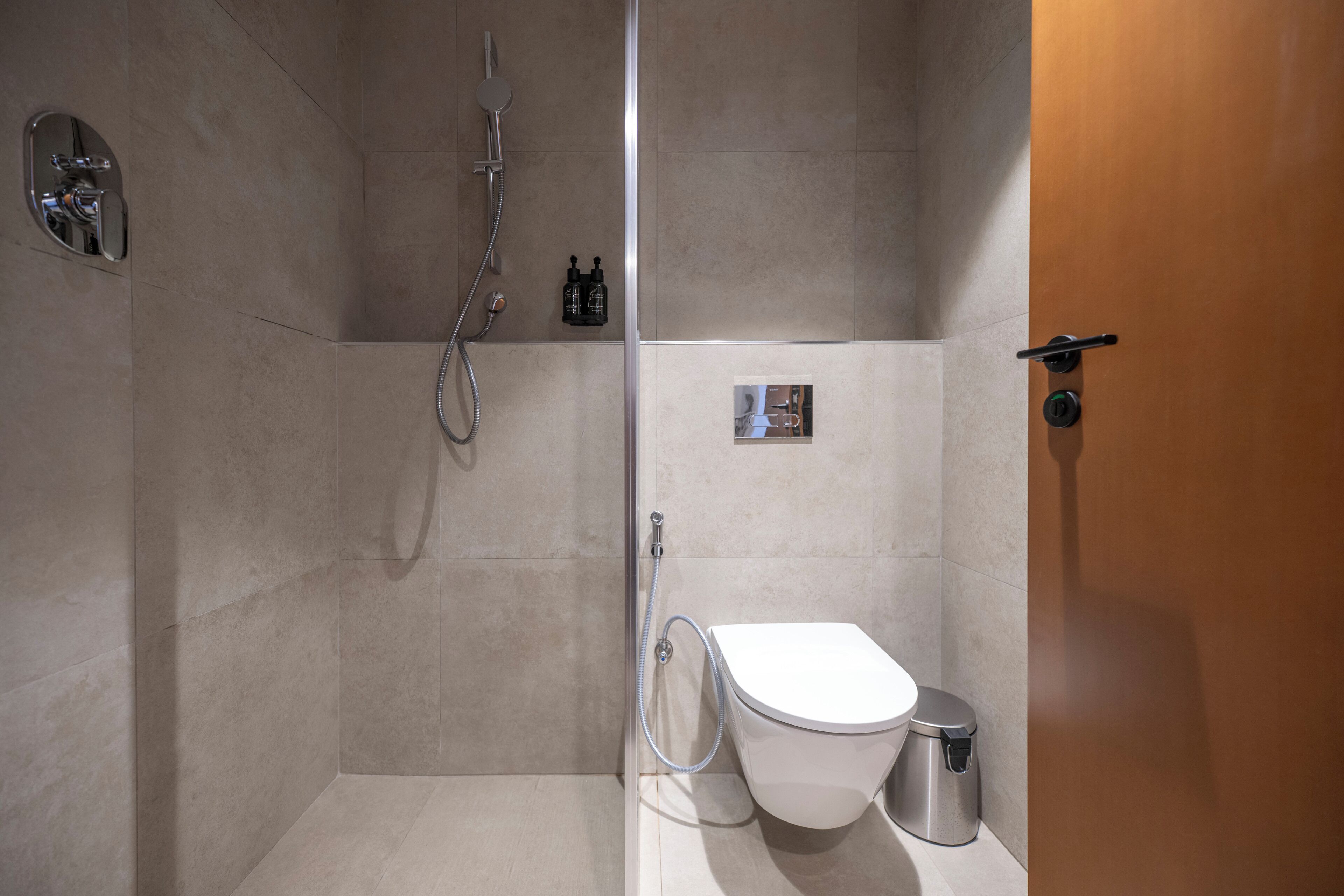 Un baño moderno con ducha, inodoro y un pequeño cubo de basura.