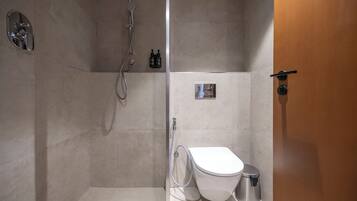A modern bathroom with a shower, toilet, and a small trash bin.